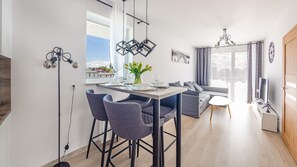 A modern kitchen with a dining area, a sofa, and a TV. - Sun & Snow Osiedle Bursztynowe (Kolobrzeg)