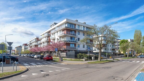 A multi-story residential building with balconies, a parking area, and a pedestrian crossing. - Apartamenty Sun&Snow Osiedle Bursztynowe (Kolobrzeg)