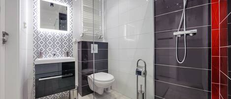 A modern bathroom with a glass shower enclosure, a white toilet, and a black sink with a mirror above it.