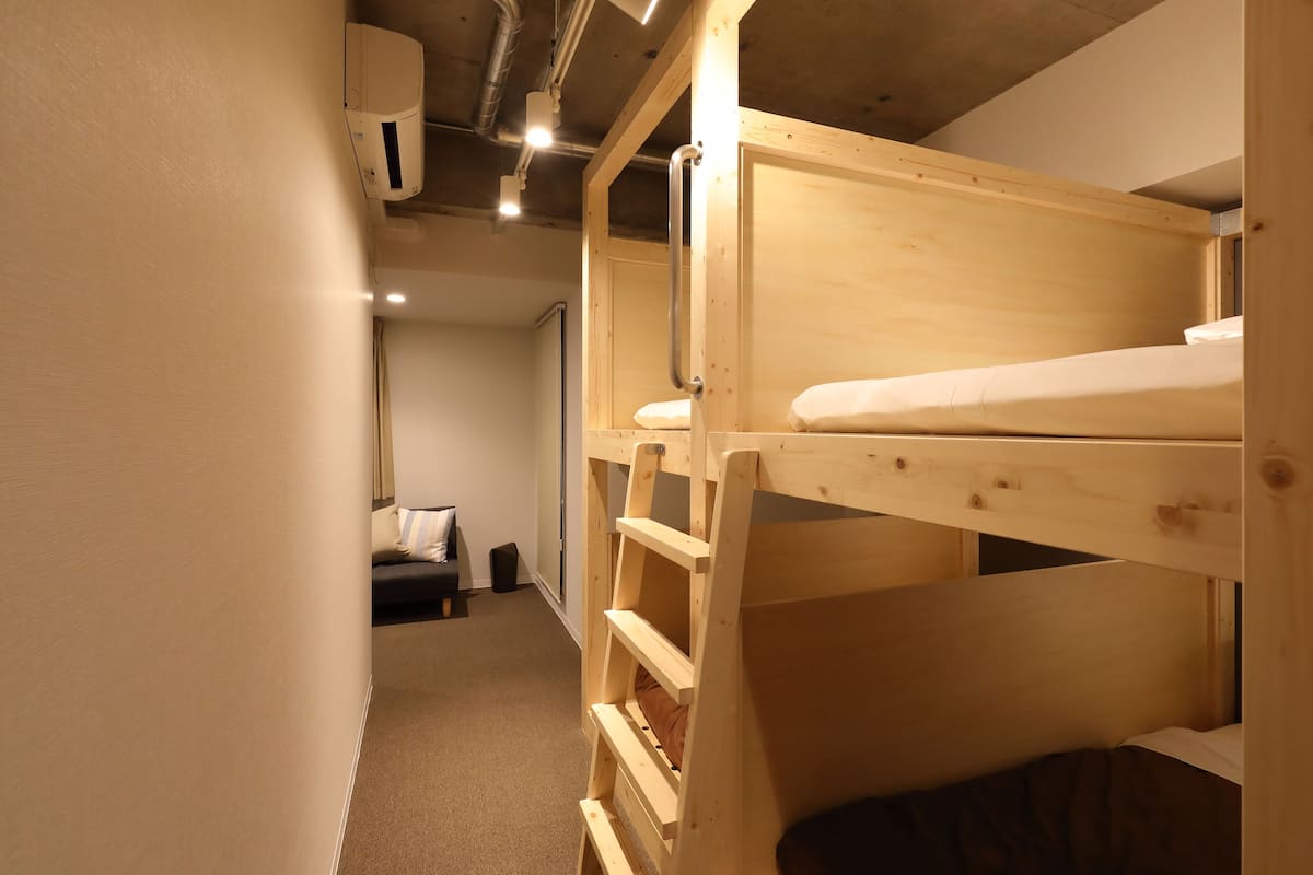 A bunk bed room with a wooden bunk bed, a small seating area with a cushion, and a door in the background.