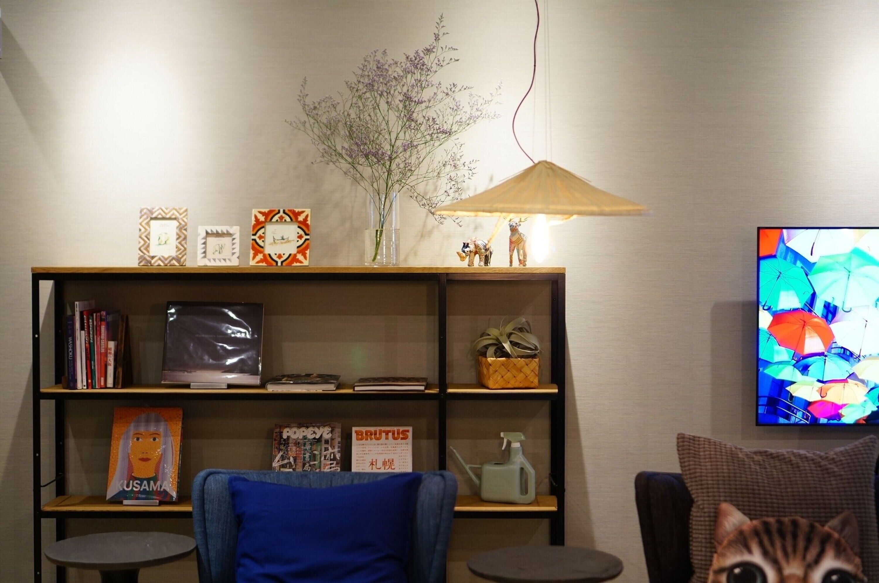 A living room with a bookshelf, a small table, a blue chair, a cat, and a TV displaying colorful umbrellas.