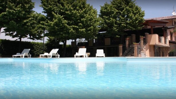 Ein Swimmingpool mit Liegestühlen und ein Gebäude mit einem Ziegeldach im Hintergrund.