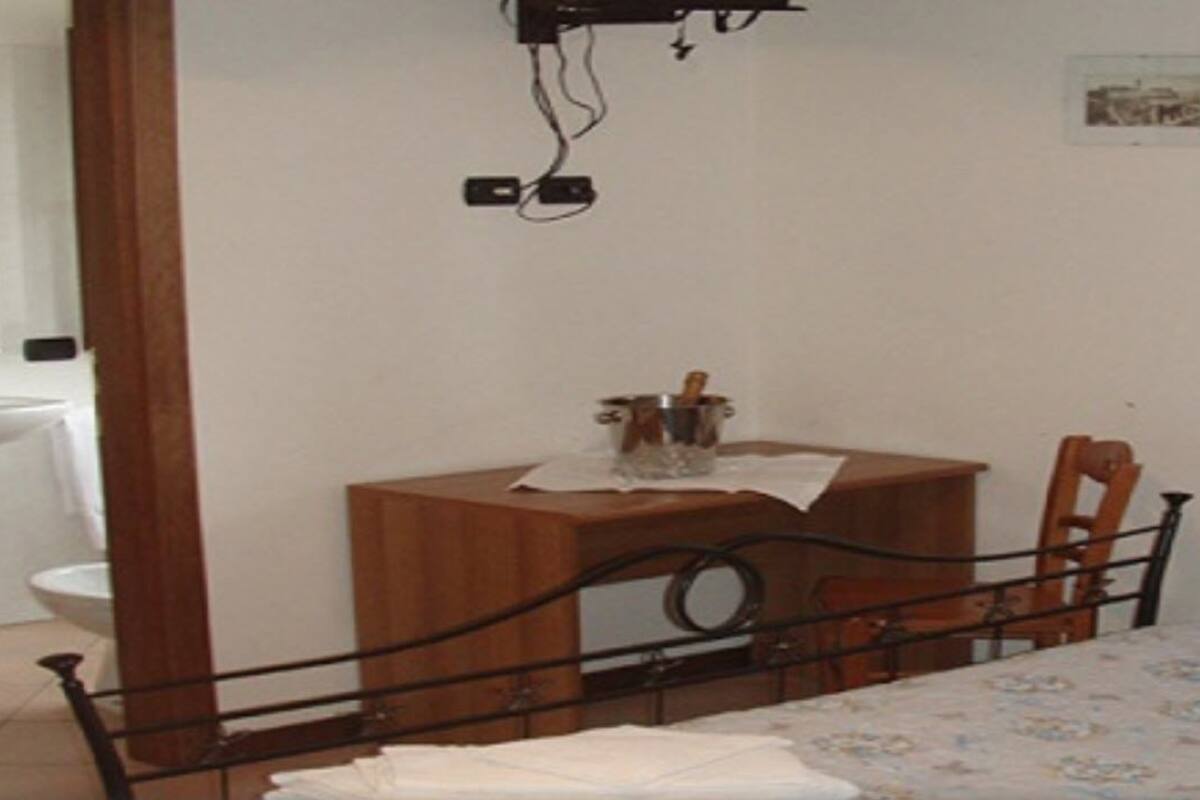 Een slaapkamer met een bed, een houten nachtkastje, een klein tafeltje met een lamp, een witte wastafel en een spiegel.