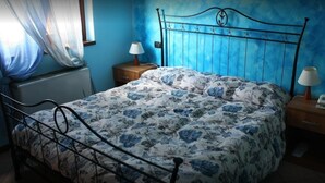 Ein Schlafzimmer mit Bett, Nachttisch, Lampe und einem Fenster mit Vorhängen.