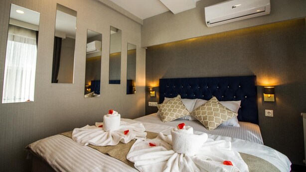 Une chambre d’hôtel avec un grand lit, plusieurs oreillers, une tête de lit dotée de lampes et un appareil de climatisation.