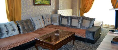 A living room with a sectional sofa, a glass coffee table, a white armchair, and a patterned carpet.
