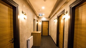 Un couloir avec des portes en bois, un radiateur et des luminaires fixés au mur.