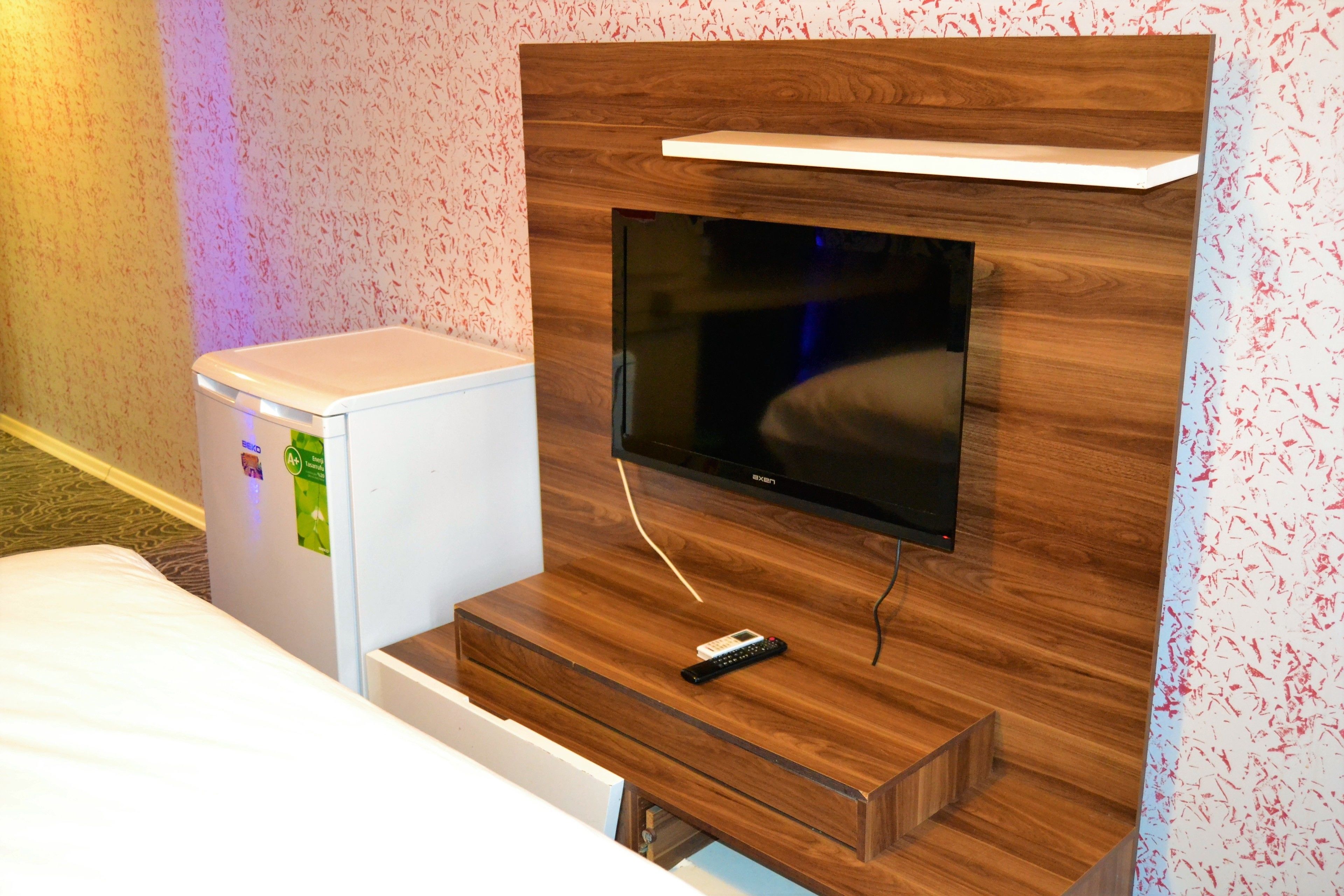 A hotel room with a wooden TV stand, a flat-screen TV, a small refrigerator, and a bed.