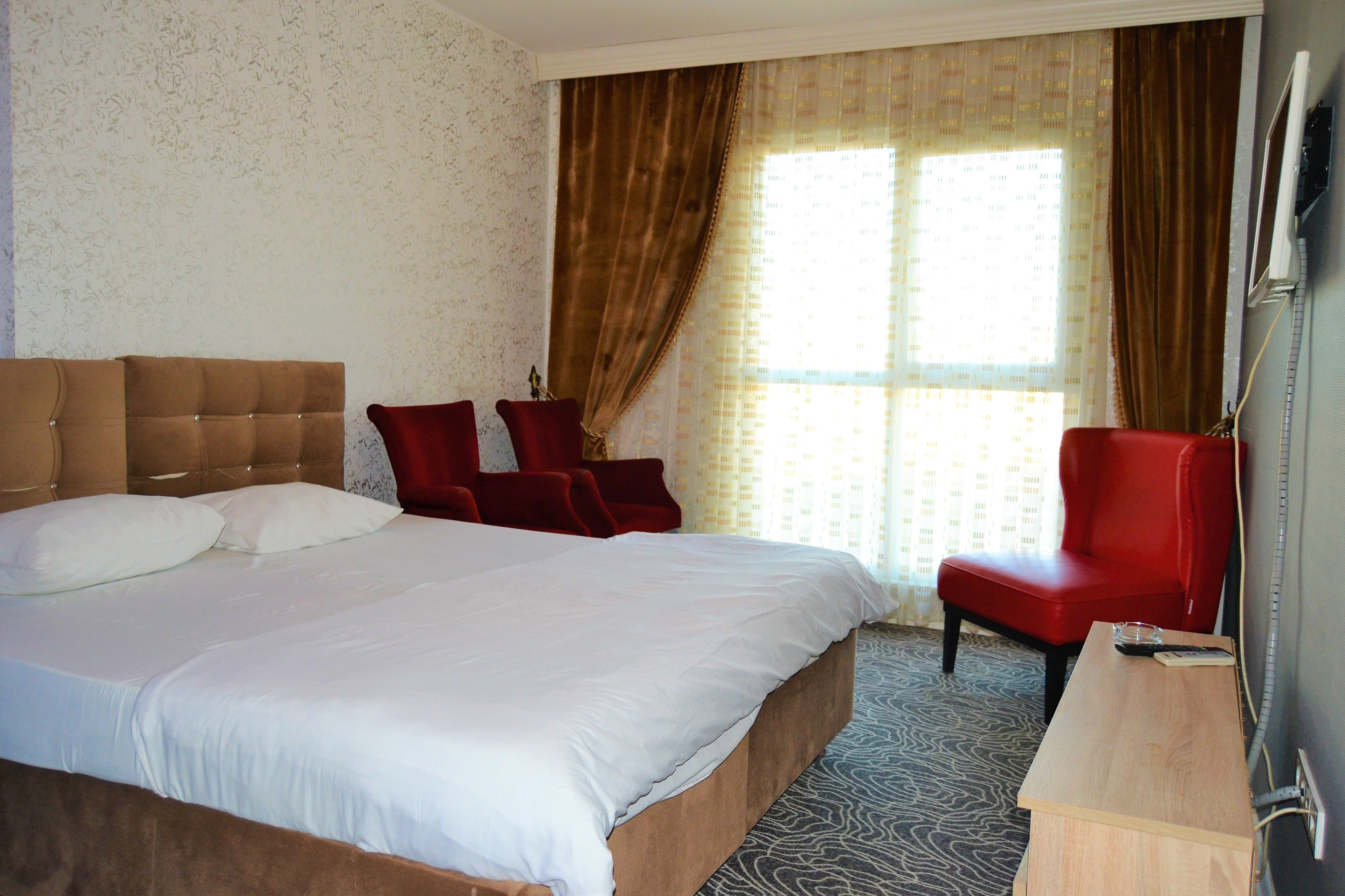 A hotel room with a large bed, two red chairs, a wooden side table, and a television.
