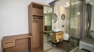 A modern bedroom with a wooden desk, a glass-enclosed shower, and a grey sofa.