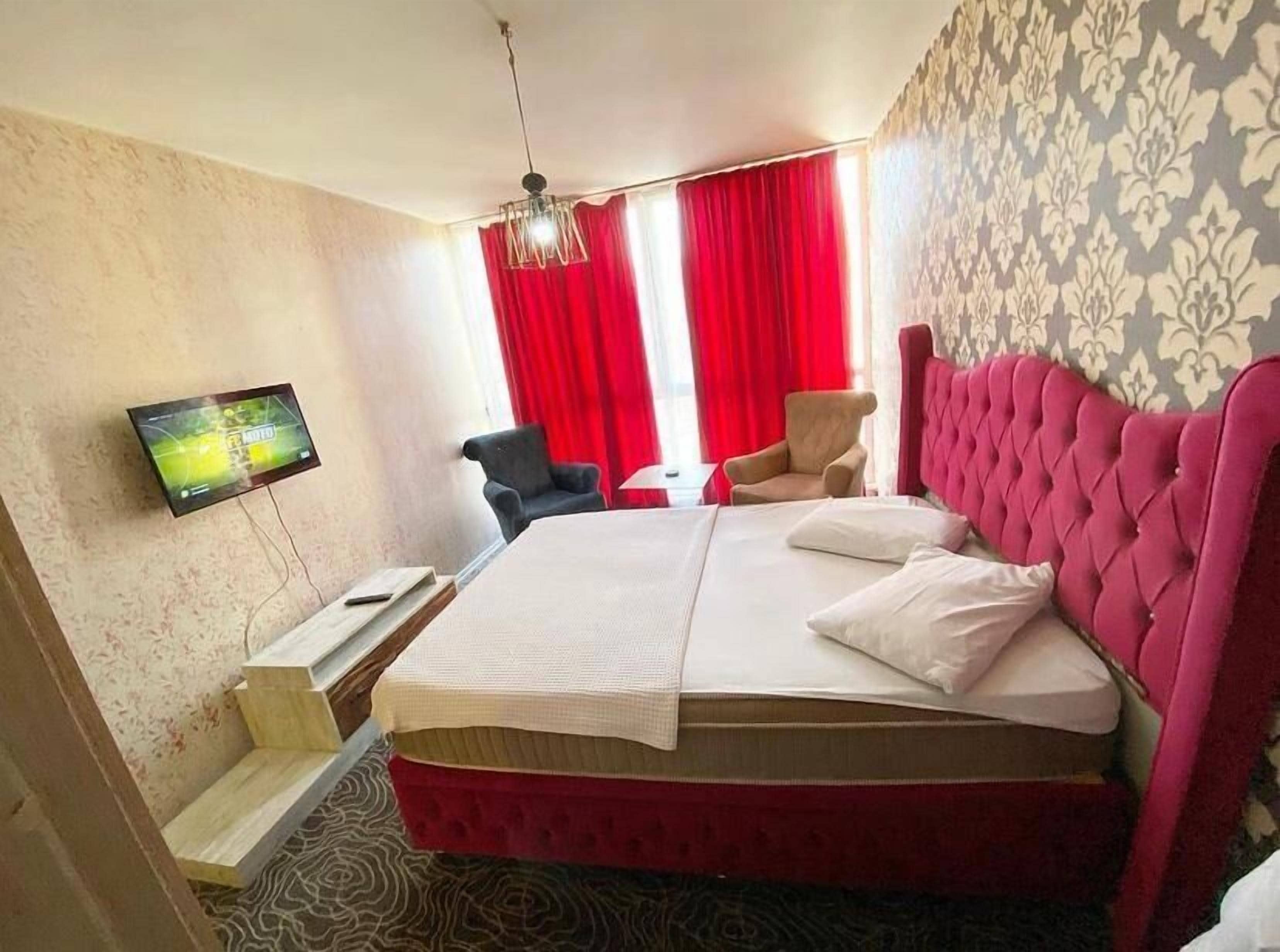 Una habitación de hotel con una cama grande, un televisor de pantalla plana montado en la pared, un escritorio con una silla y una cortina roja.