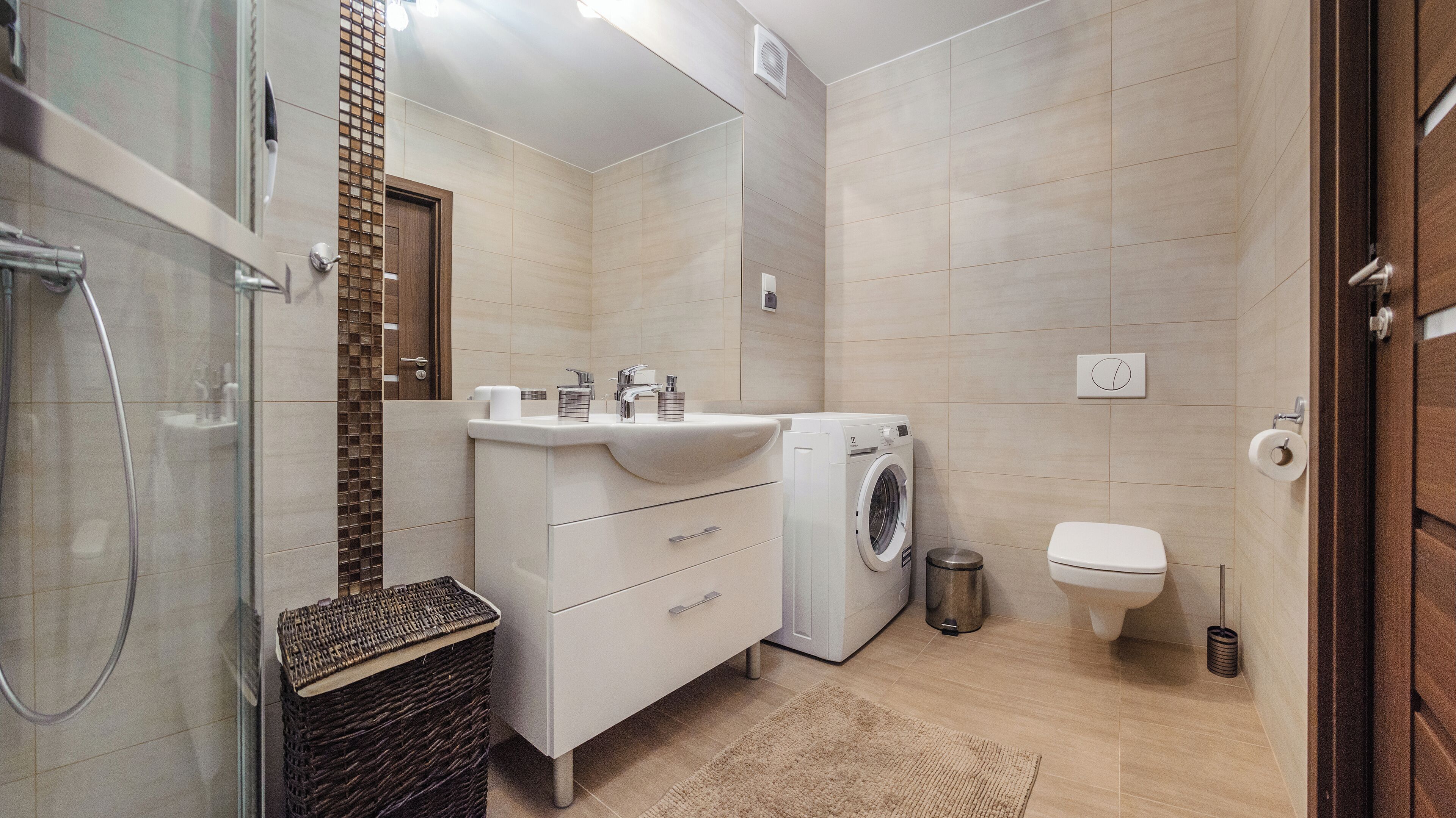 A modern bathroom with a washing machine, toilet, and a glass shower enclosure.