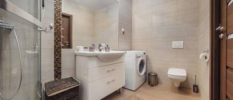 Ein modernes Badezimmer mit Waschmaschine, Toilette und einer Duschkabine aus Glas.