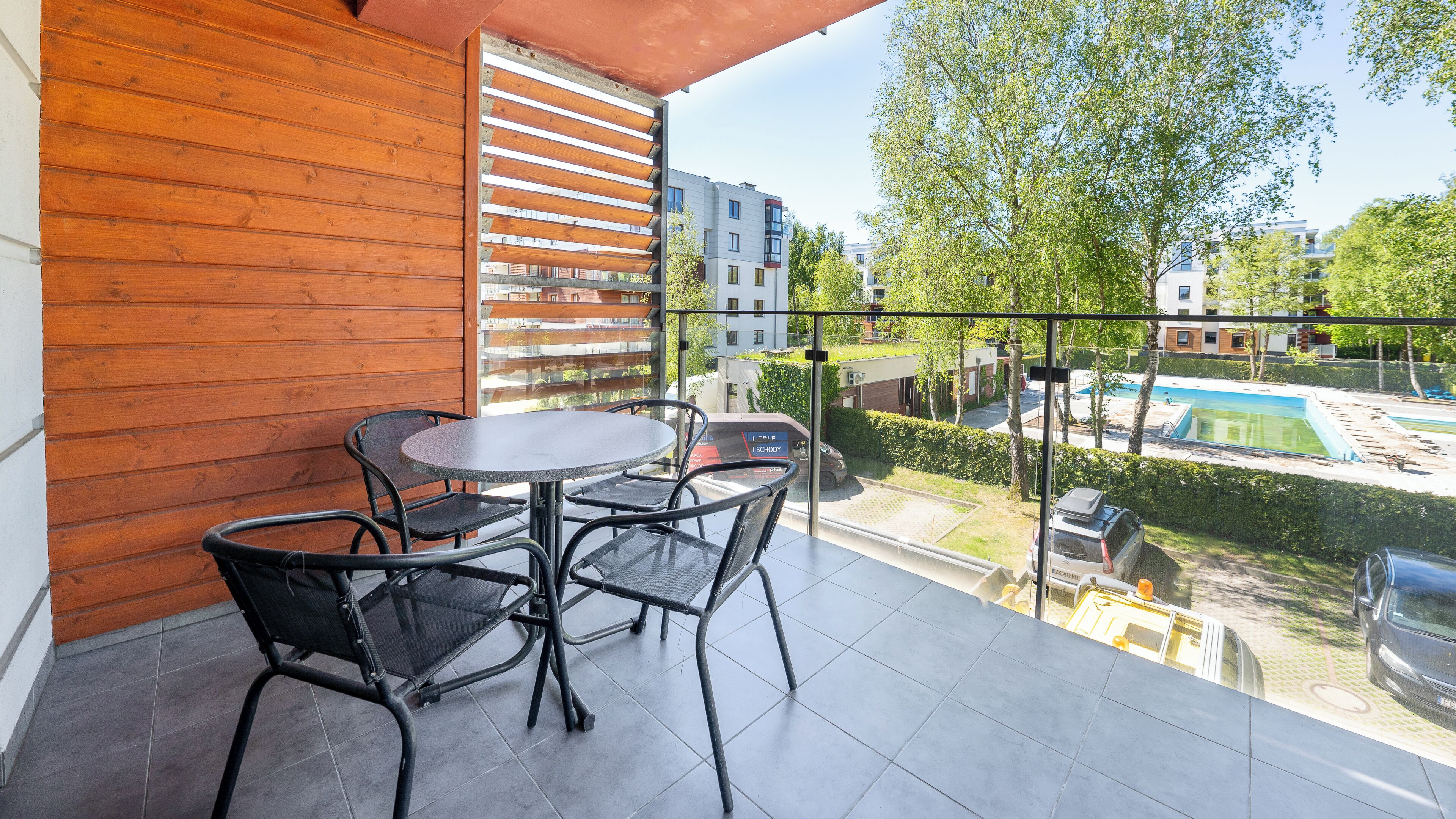 En balkon med trævæg, et rundt bord og fire stole.