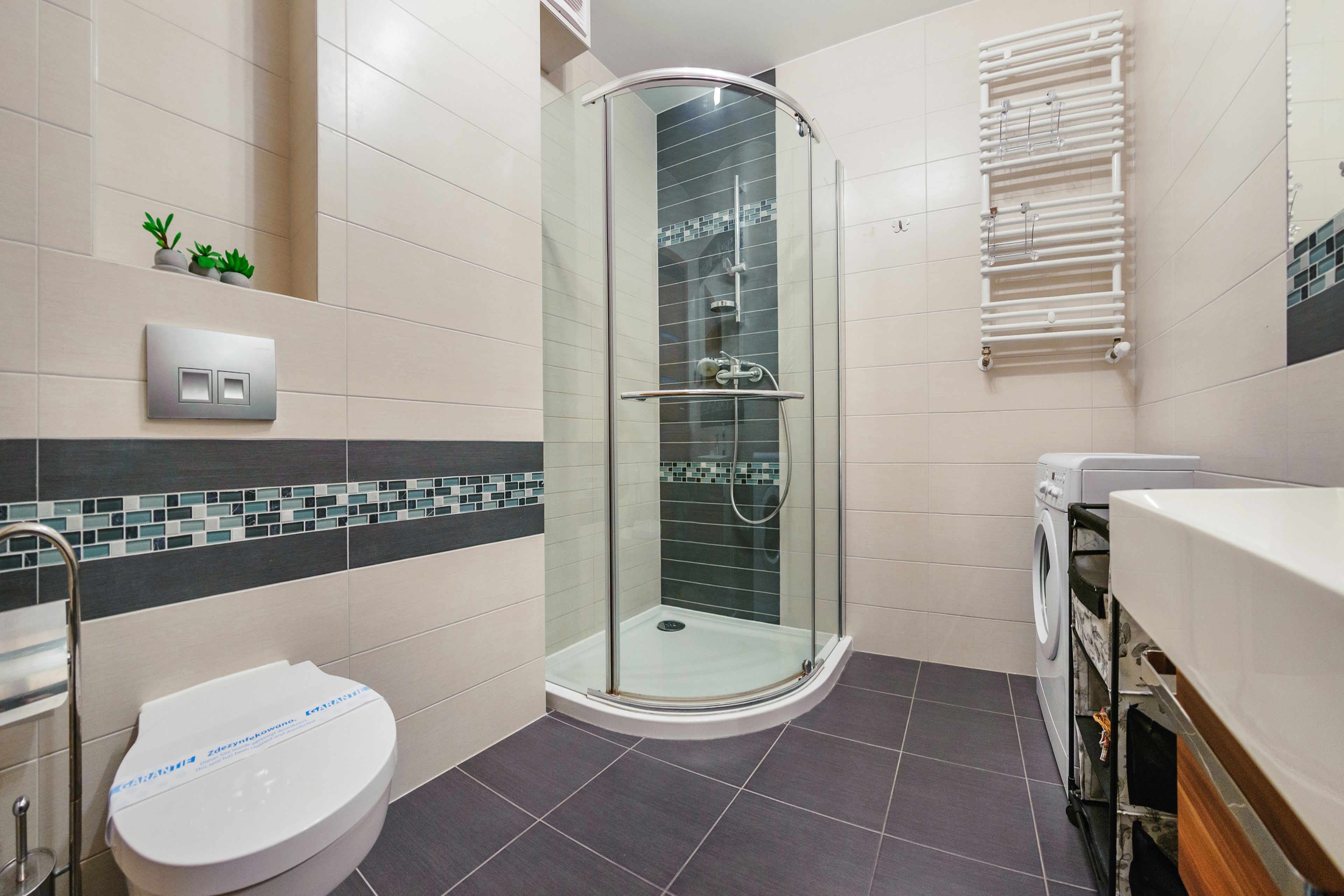 A modern bathroom with a glass-enclosed shower, a toilet, a washing machine, and a towel rack.