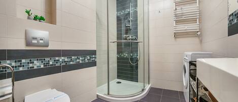 A modern bathroom with a glass-enclosed shower, a toilet, a washing machine, and a towel rack.