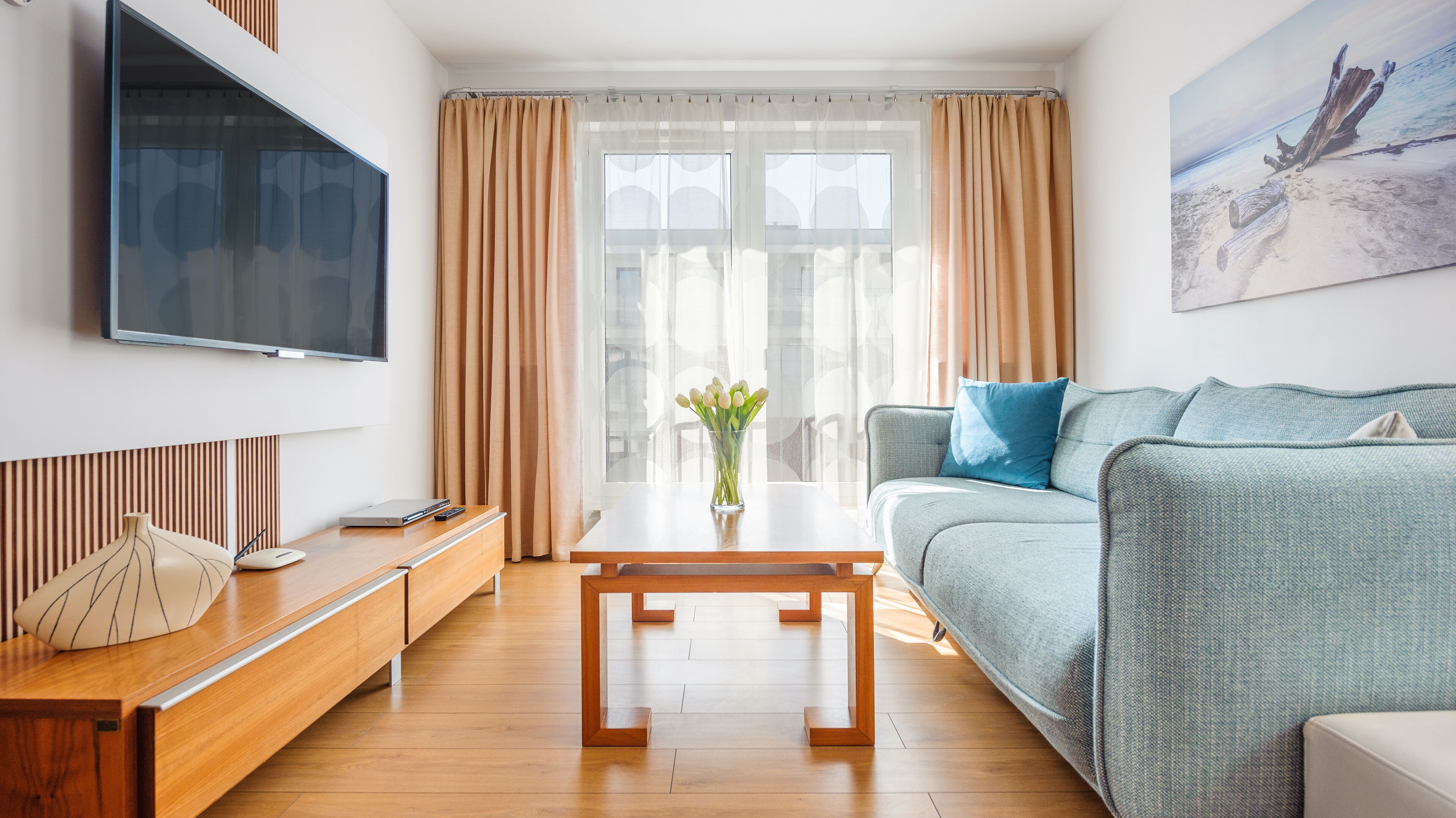 Ein modernes Wohnzimmer mit einer Couch, einem Couchtisch, einem Fernseher und einem Fenster mit Vorhängen.
