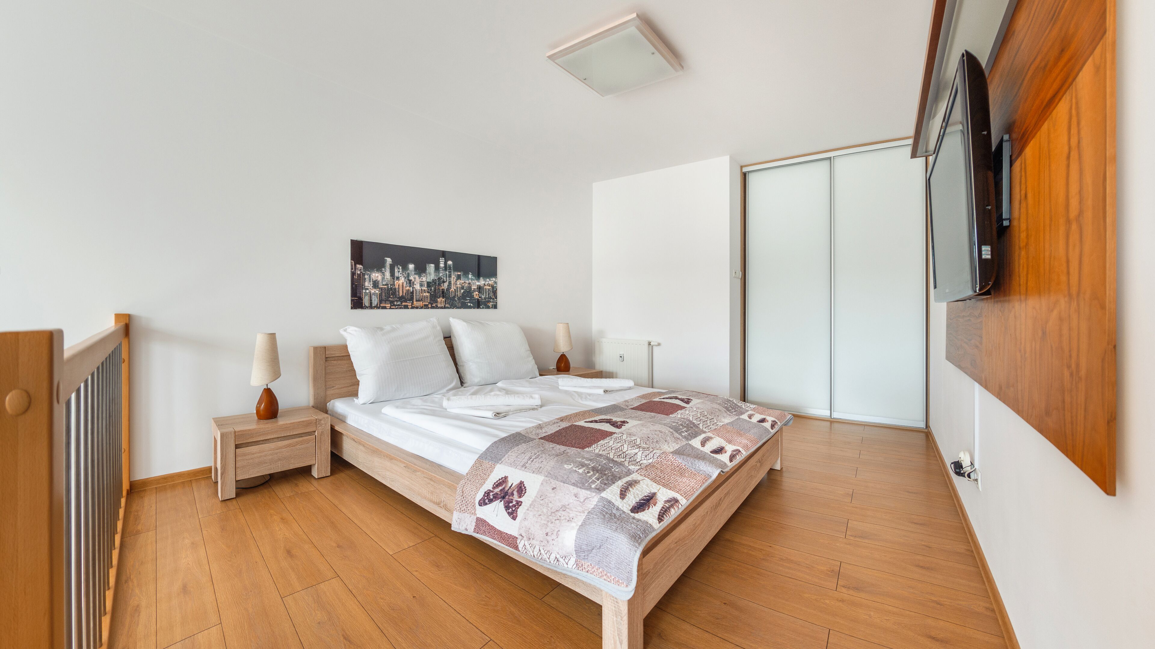 Une chambre à coucher avec un lit en bois, du linge de lit blanc, un tableau représentant un paysage urbain, une lampe de chevet et une armoire.