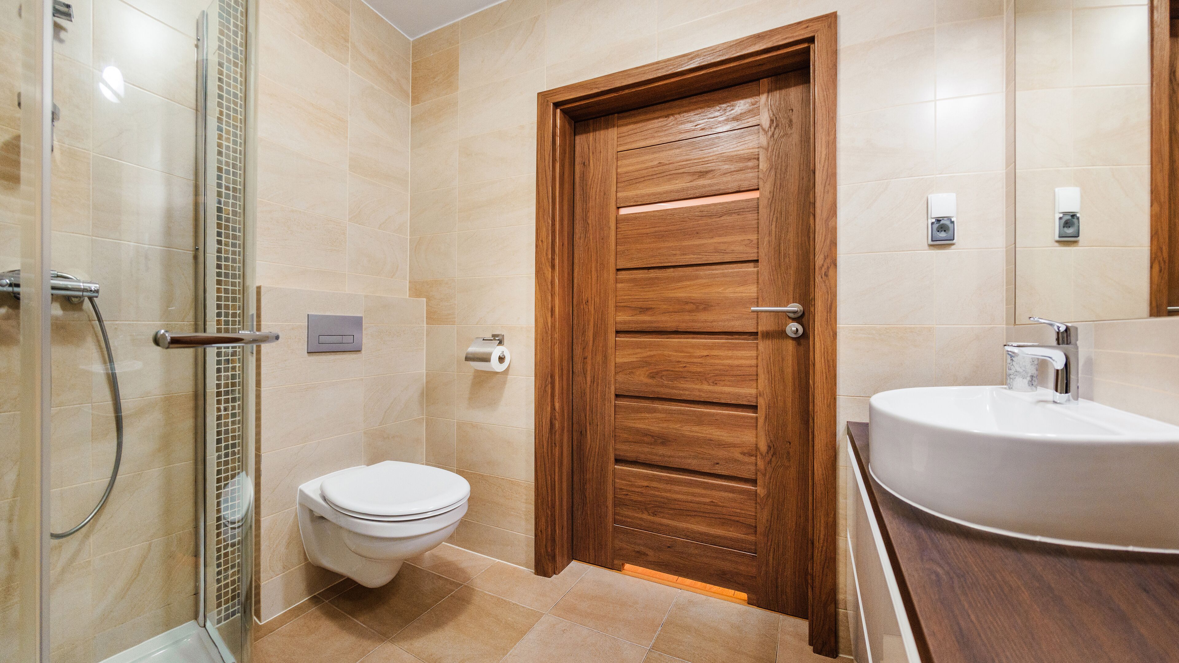 Un baño con puerta de madera, un inodoro, ducha y lavamanos.