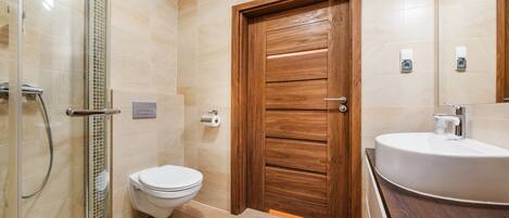 Un baño con puerta de madera, un inodoro, ducha y lavamanos.
