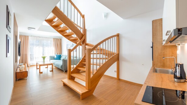 A modern apartment with a wooden staircase, a kitchen with a built-in oven, a living area with a sofa and a coffee table, and a large window with curtains. - Apartamenty Sun & Snow Polanki (Kolobrzeg)