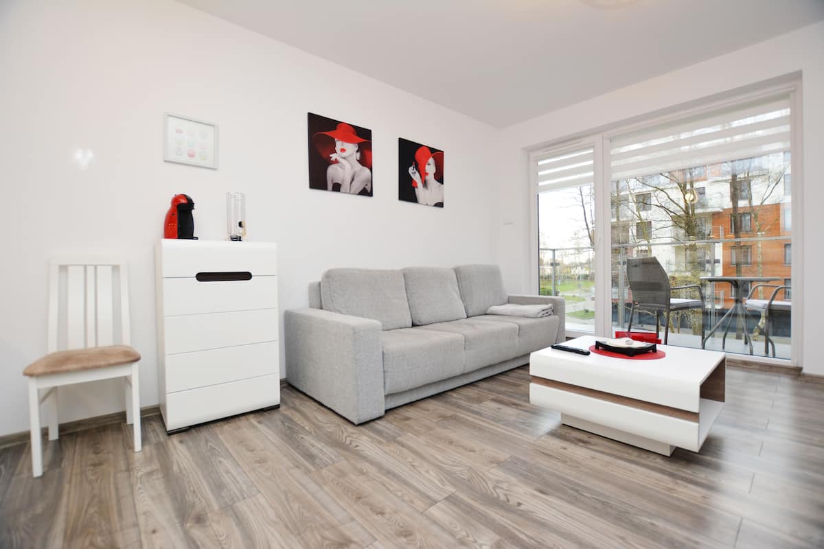 Ein modernes Wohnzimmer mit einem grauen Sofa, einer weißen Ablage und einem Glastisch mit einem roten Gegenstand darauf.