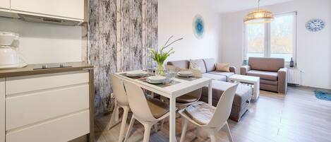 A modern kitchen with white cabinets, a dining table set with plates and glasses, and a living area with a sofa and a window with a view.