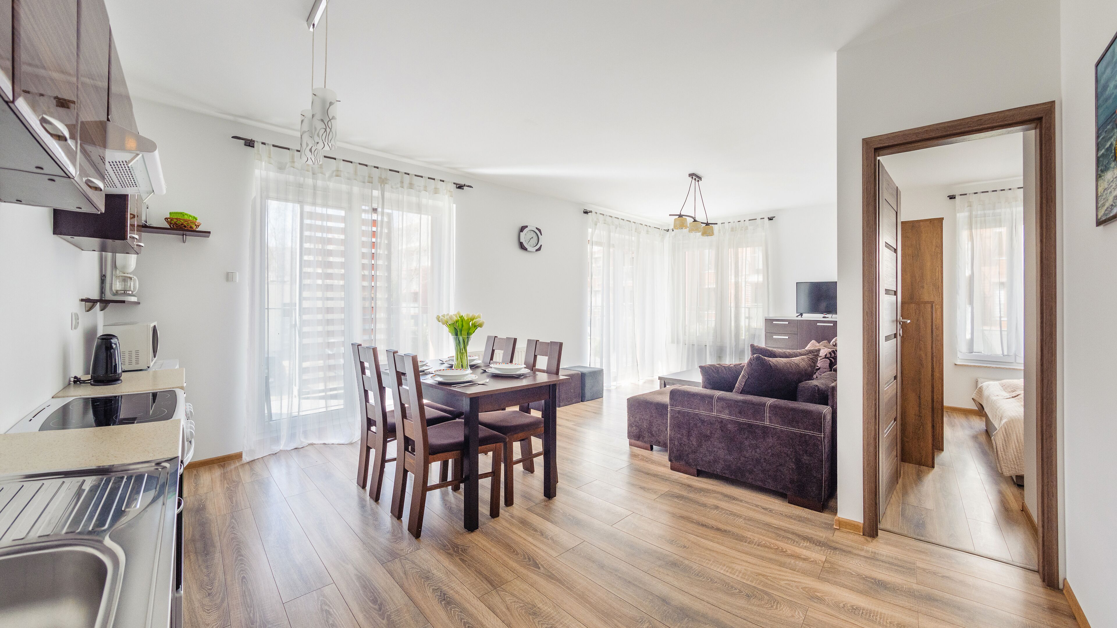 A modern kitchen with a built-in oven, a dining area with a table and chairs, a sofa, and a TV in the living room.
