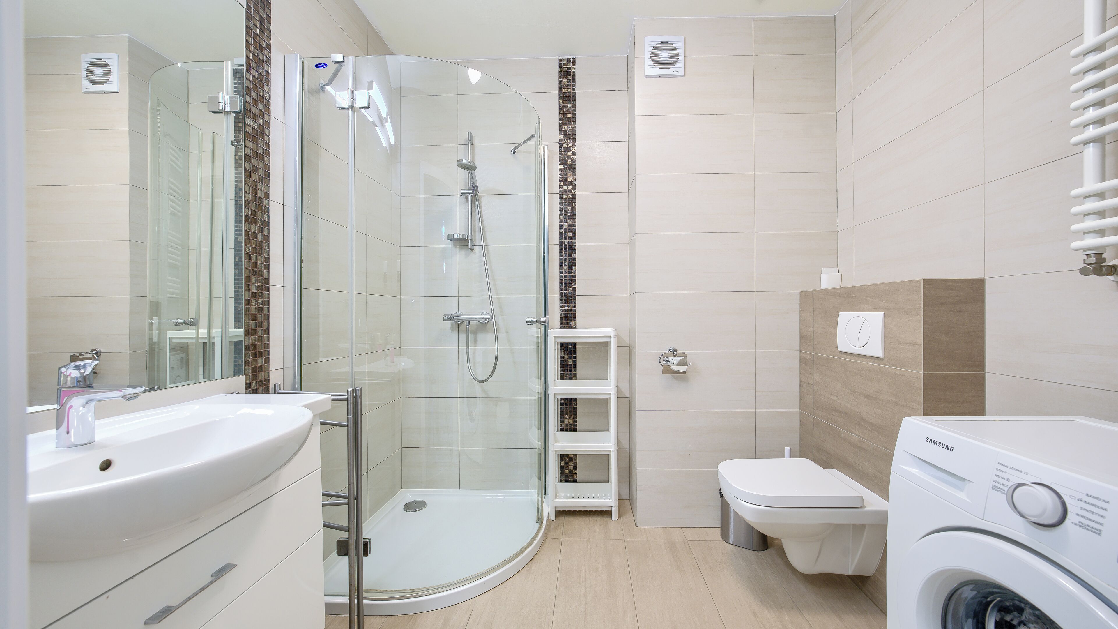 Een moderne badkamer met een glazen douchecabine, een wastafel, toilet en een wasmachine.