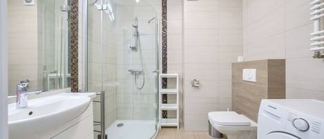 Une salle de bain moderne avec une douche à parois de verre, un lavabo, des toilettes et un lave-linge.