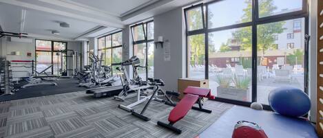 A gym with various exercise equipment, large windows, and a view of the outside.