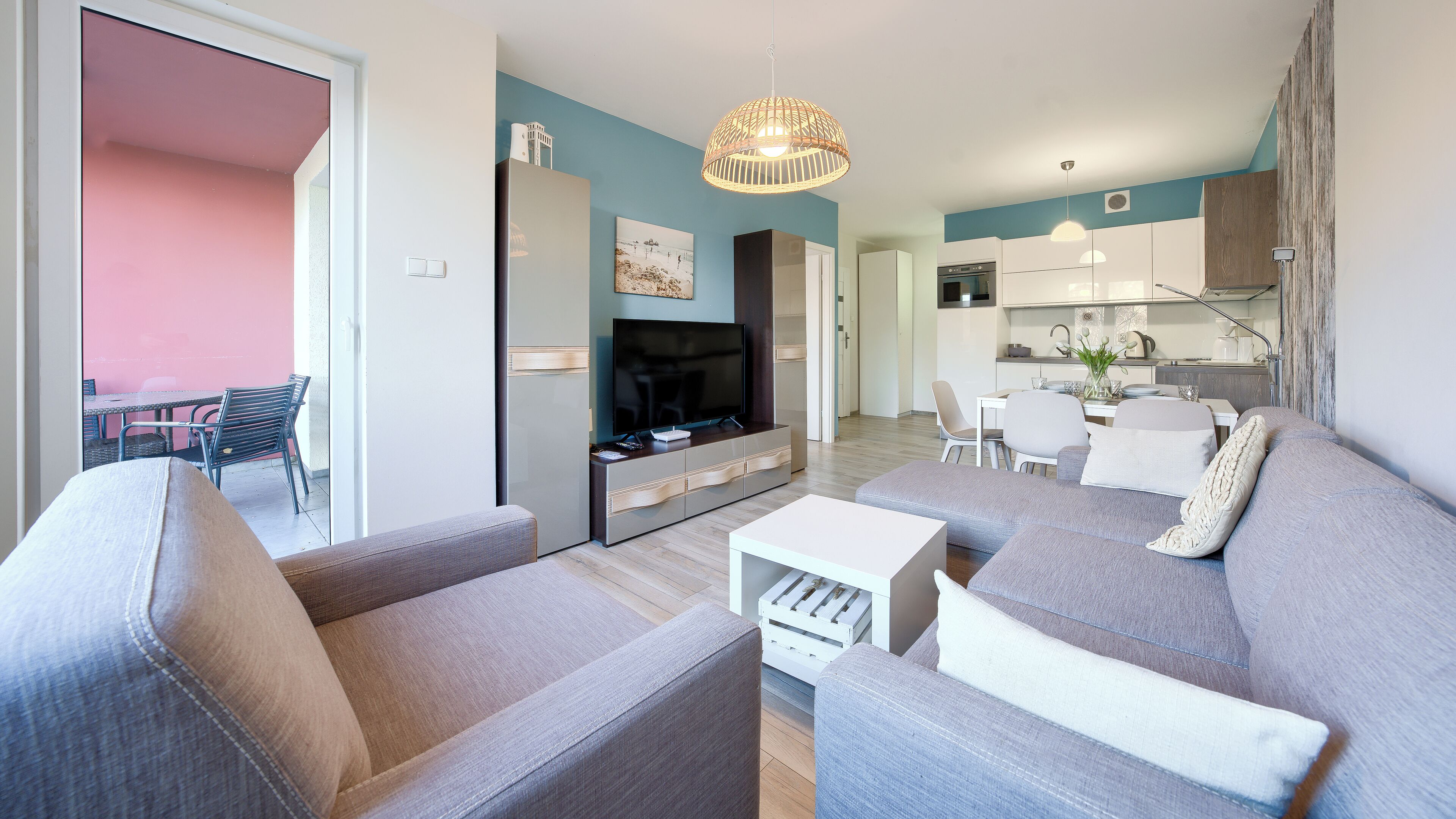 Una sala de estar moderna con un sofá gris, un televisor y un comedor con mesa y sillas.