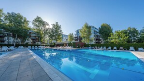 A swimming pool with lounge chairs and a building with multiple balconies in the background. - Apartamenty Sun & Snow Polanki (Kolobrzeg)