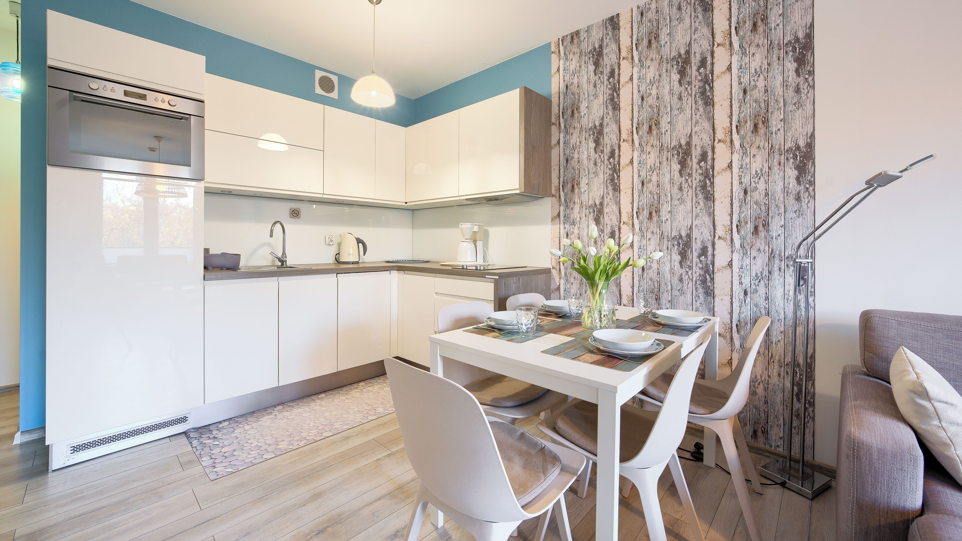 A modern kitchen with white cabinets, a built-in oven, and a dining area with a table set for two.