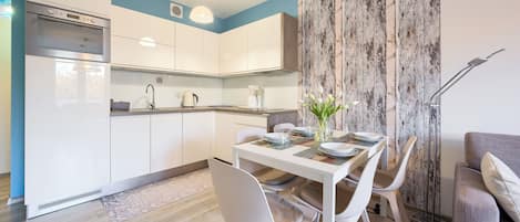 Una cocina moderna con armarios blancos, horno empotrado y comedor con mesa para dos.
