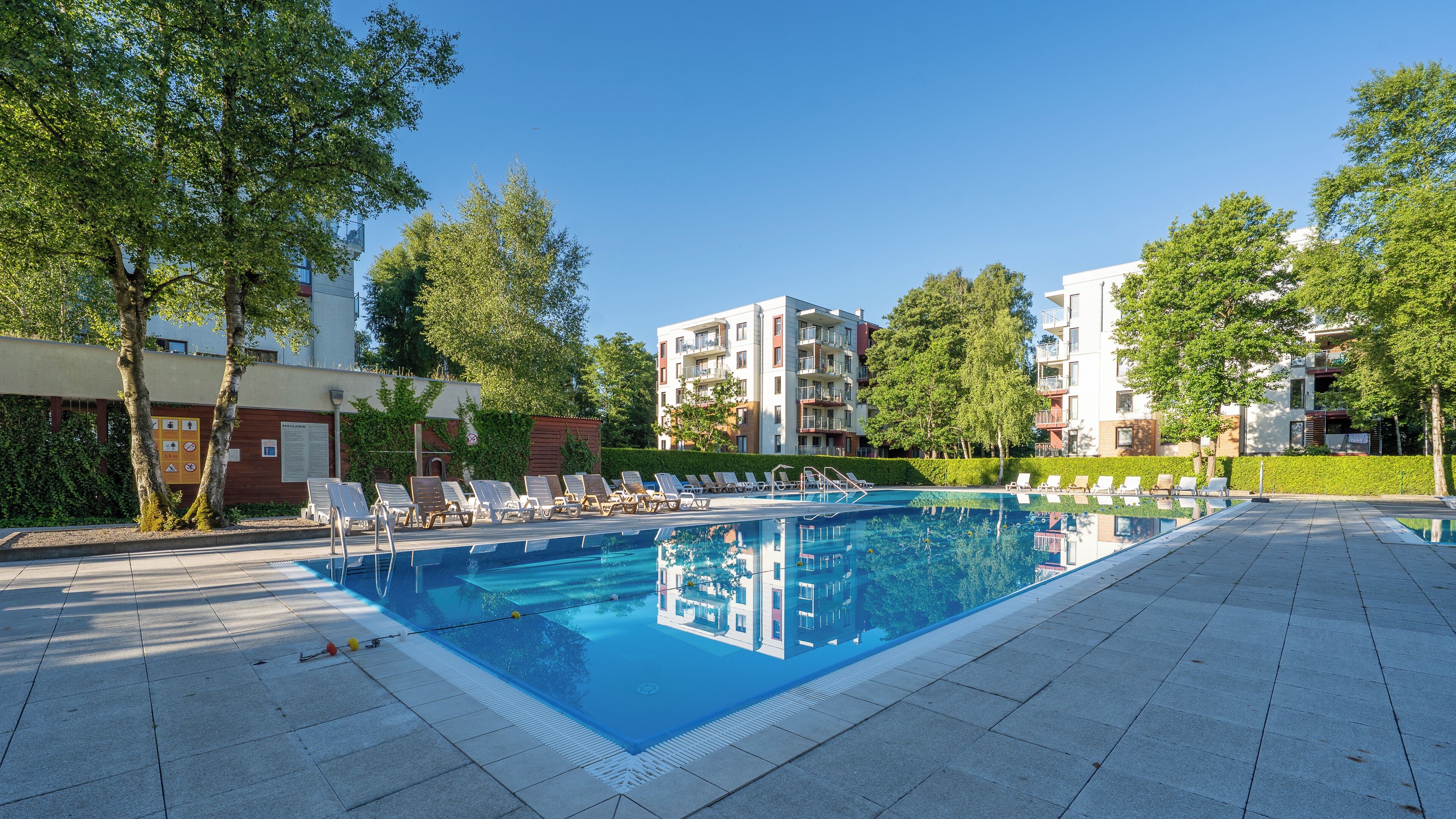 Ein Schwimmbad mit Liegestühlen, umgeben von Bäumen und modernen Wohngebäuden.