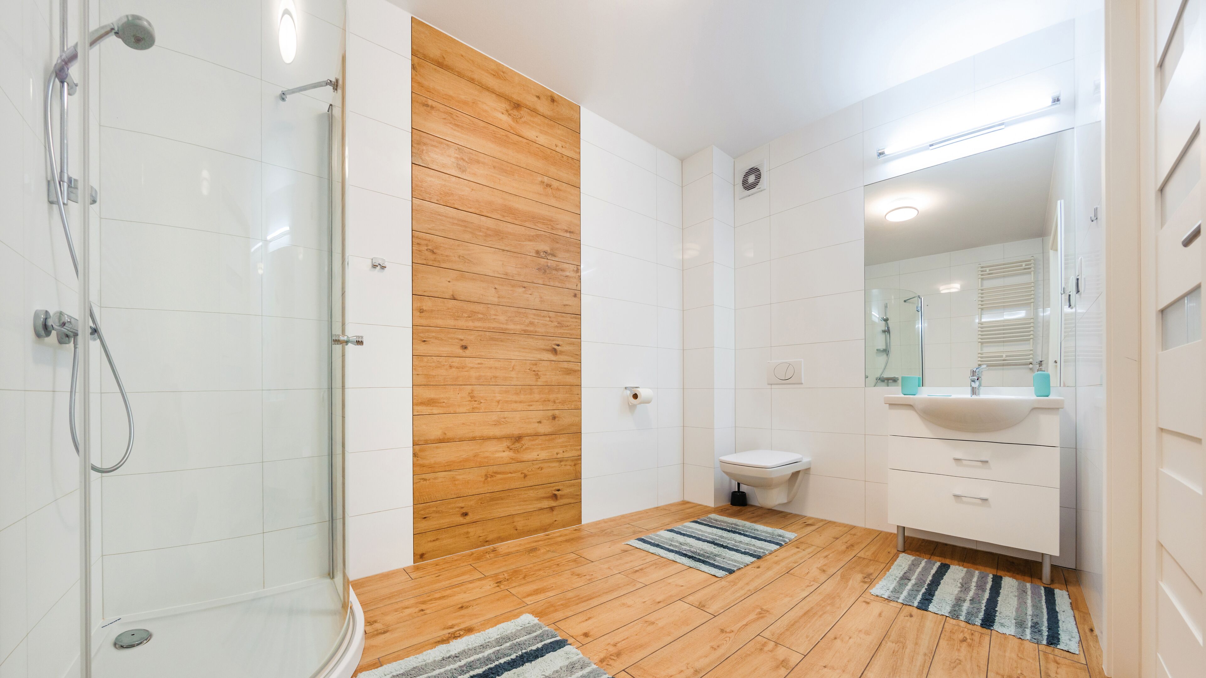 Un baño moderno con cabina de ducha de vidrio, pared decorativa de madera, inodoro blanco y lavamanos con espejo.