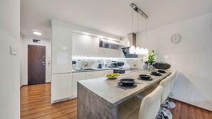 A modern kitchen with white cabinets, a marble countertop, and a dining area with a white chair. - Apartamenty Sun & Snow Polanki (Kolobrzeg)