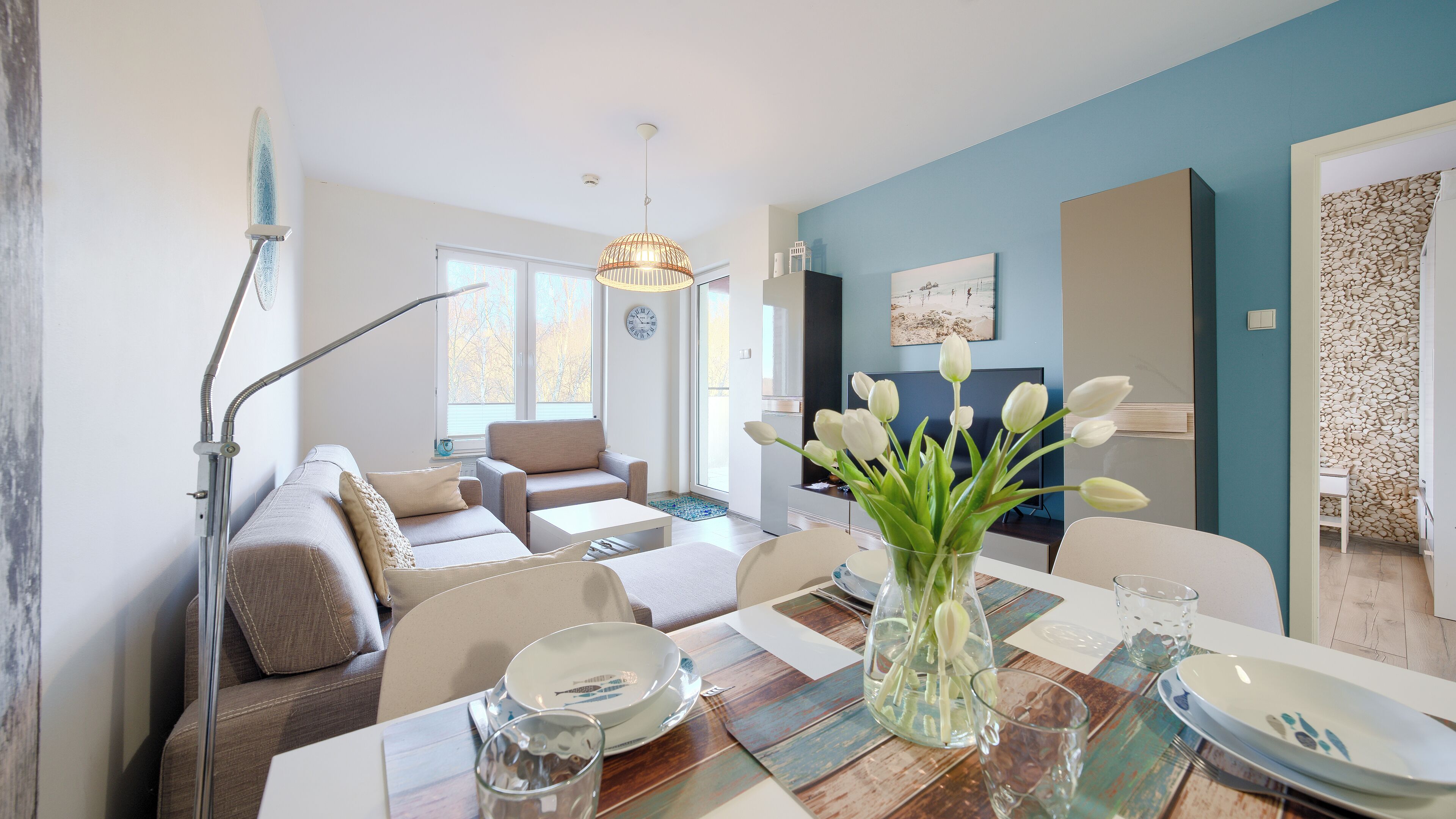 A modern living room with a sofa, coffee table, and a dining area with a table set for two.