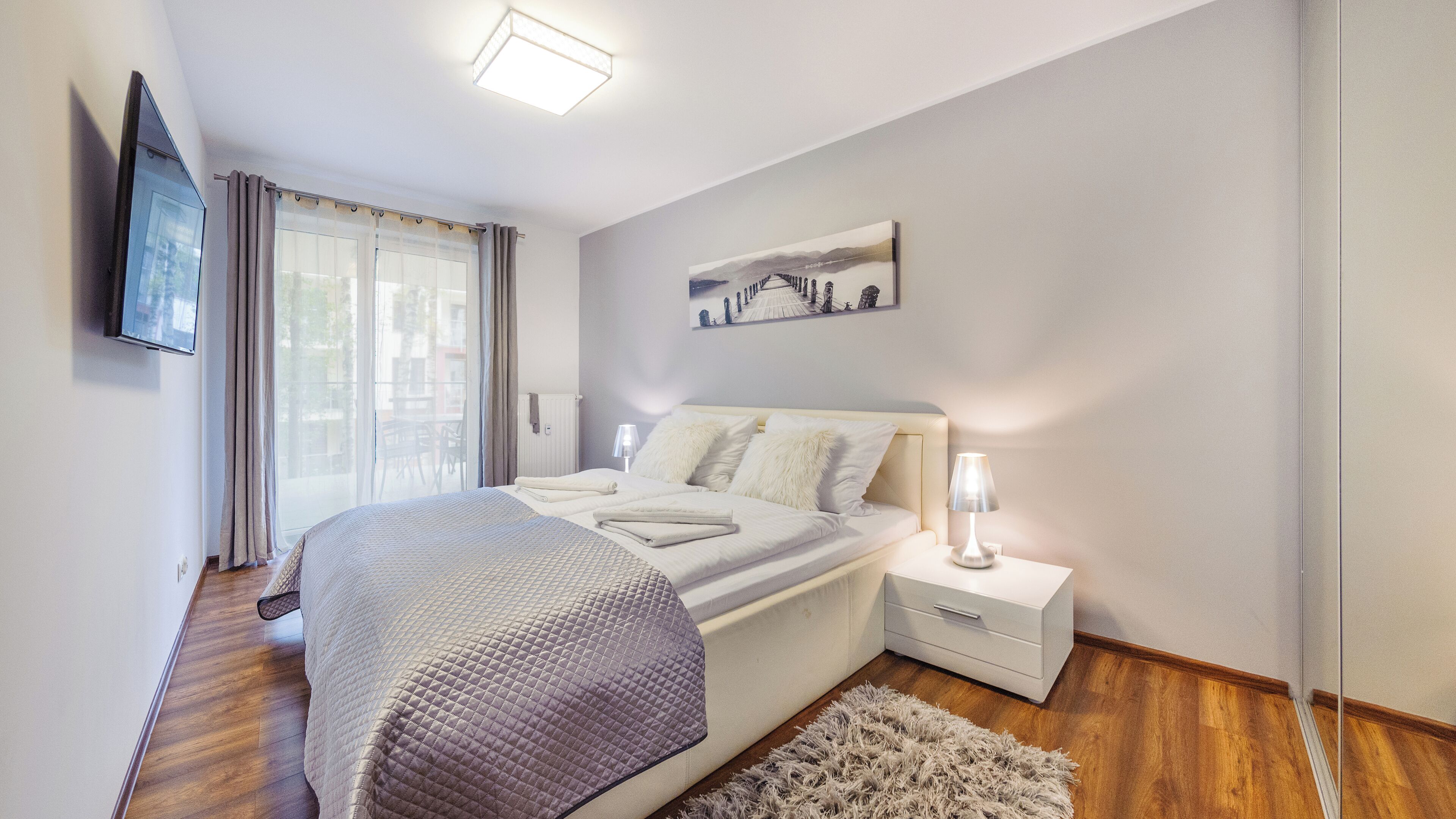 A modern bedroom with a large bed, bedside tables, a flat-screen TV, and a painting on the wall.