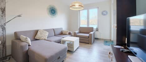 A modern living room with a grey sofa, a white coffee table, and a television on a wooden stand.