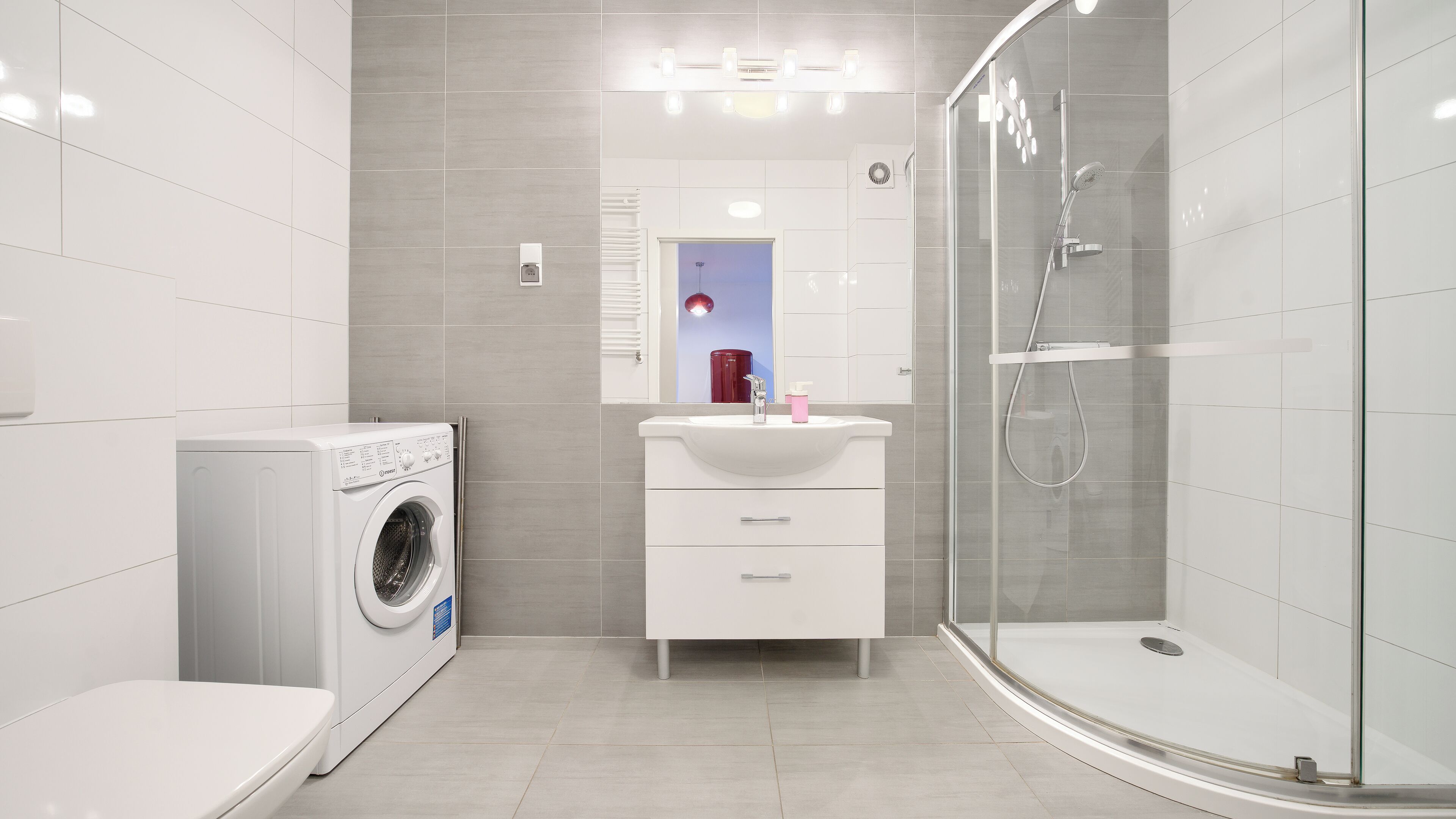 A modern bathroom with a washing machine, a sink with a mirror, and a glass-enclosed shower.
