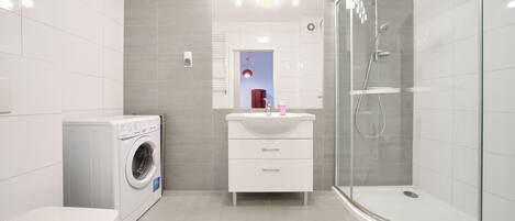 A modern bathroom with a washing machine, a sink with a mirror, and a glass-enclosed shower.