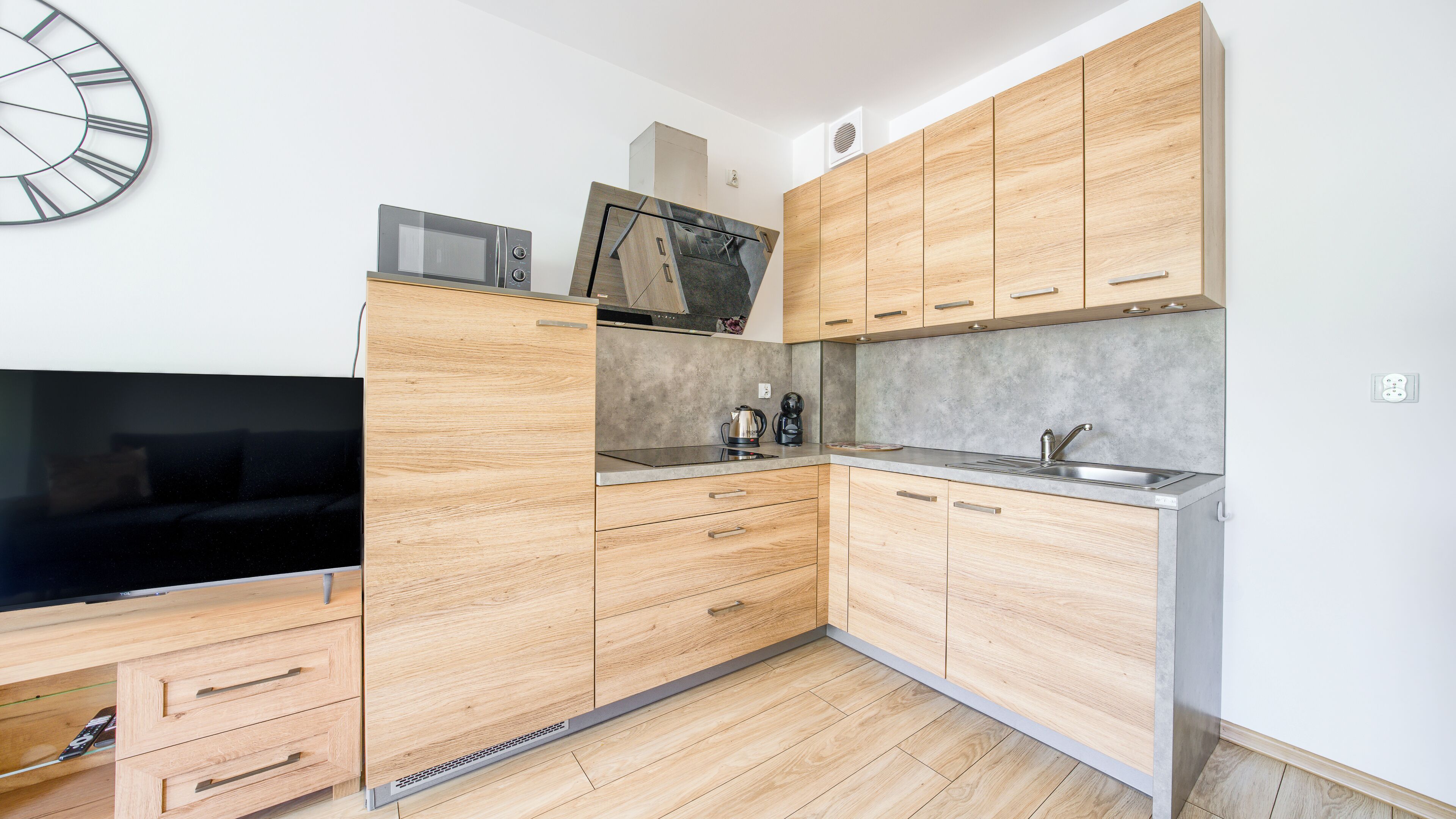 Eine moderne Küche mit Holzschränken, einer Mikrowelle, einem Wasserkocher und einem eingebauten Backofen.
