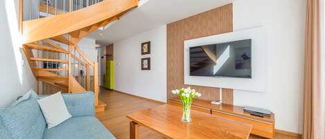 A modern living room with a wooden staircase, a flat-screen TV, a wooden coffee table, and a blue sofa.