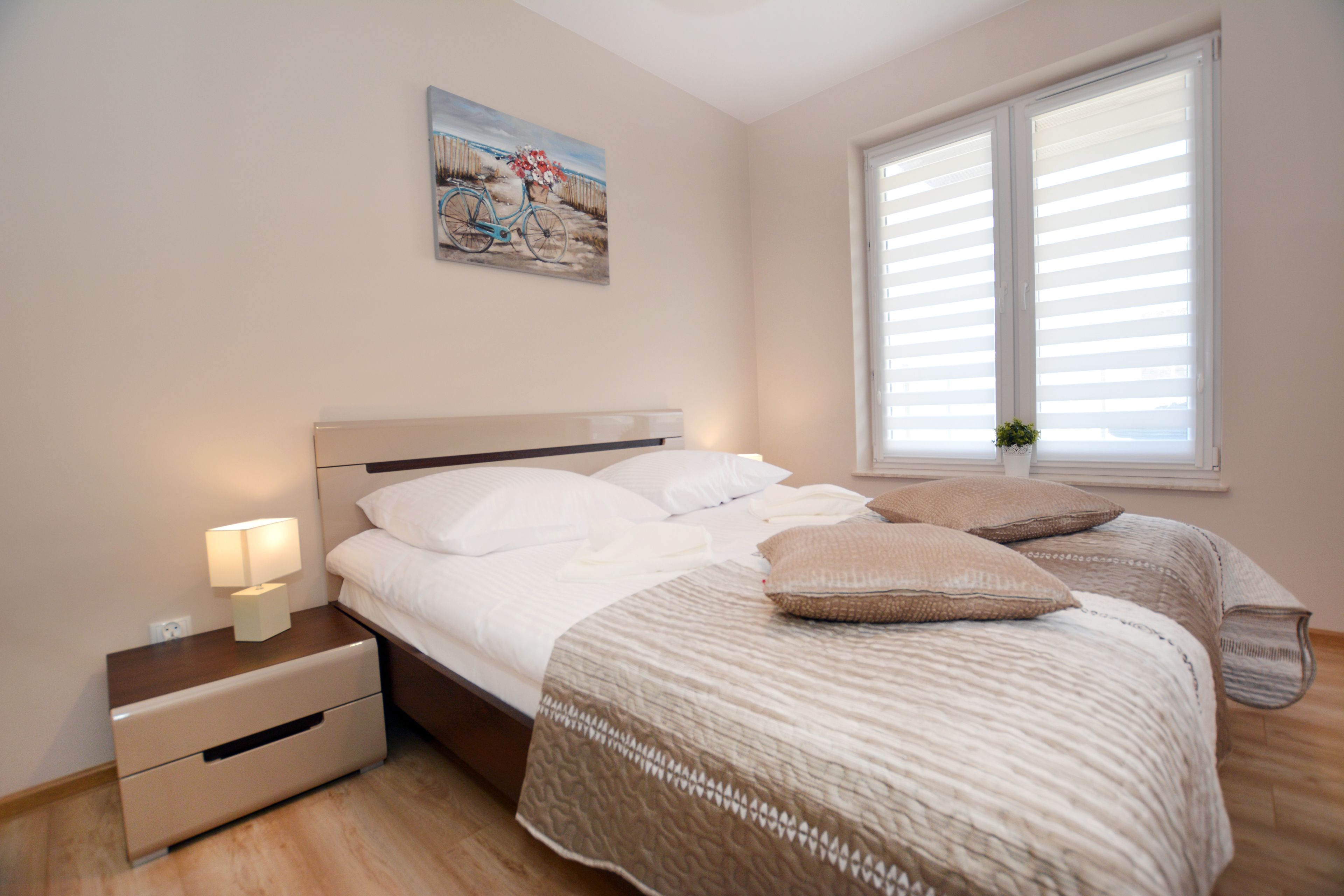 Un dormitorio con cama, mesita de noche, lámpara y ventana con persianas.
