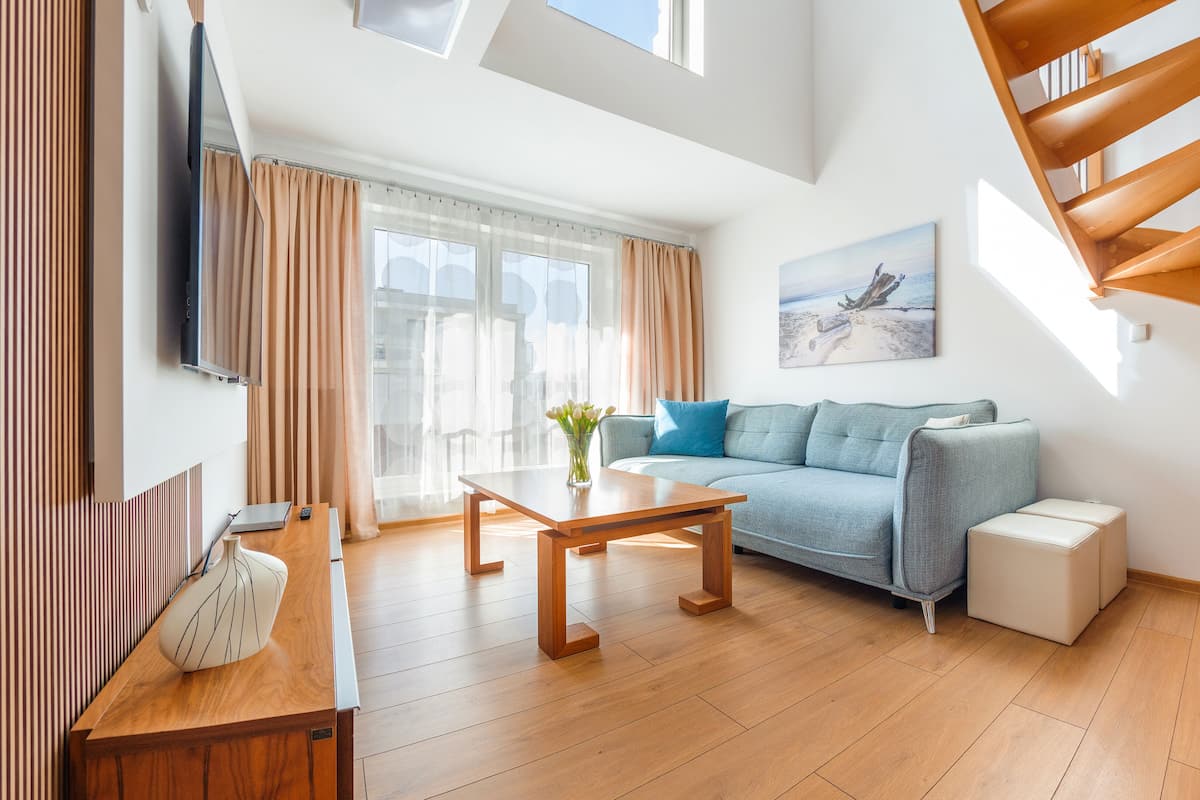 Ein modernes Wohnzimmer mit Holzboden, einer Couch, einem Couchtisch, einem Fernseher und einer Treppe.