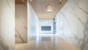 A hallway with marble walls and a polished floor, leading to a room with a large window and a wall-mounted control panel. - JTower - Isrentals (Jerusalem)