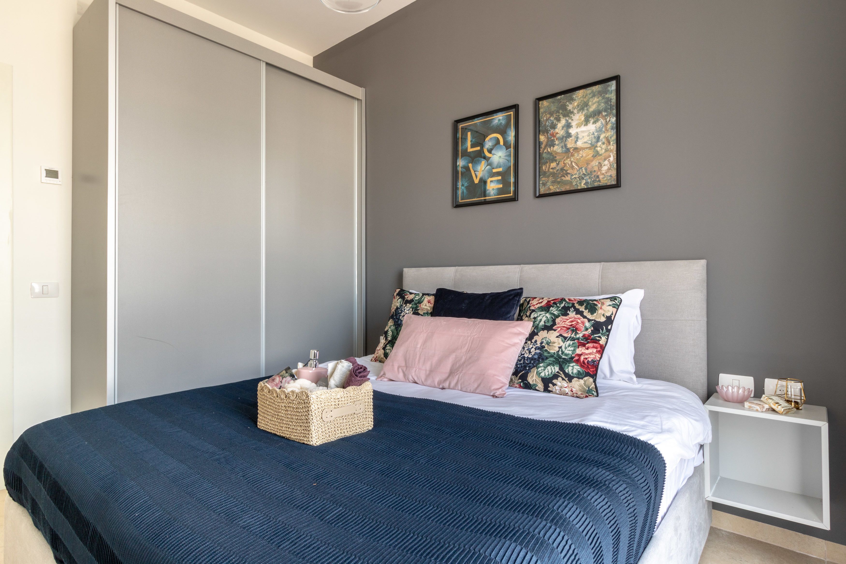 A bedroom with a bed, a bedside table, a wardrobe, and two framed pictures on the wall.