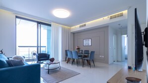 A modern living room with a blue sofa, a dining area with blue chairs, and a large window with curtains. - JTower - Isrentals (Jerusalem)